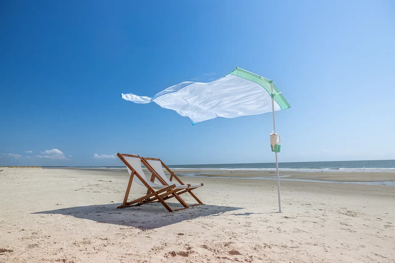 Two wooden beach chairs under a green-trim ShoreShade sail on an empty beach, ocean behind